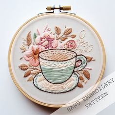 a embroidery pattern with a coffee cup and flowers on the front is featured in an embroidered hoop