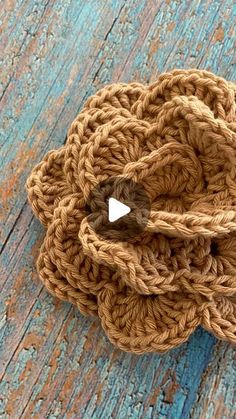 a crocheted flower with a white center on a blue wooden surface, ready to be used as a brooch