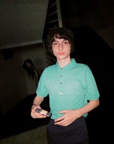 a young man in a green shirt is holding a cell phone and looking at the camera