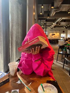 a person sitting at a table with a book in front of their face and reading