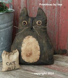 a cat pillow sitting next to a potted plant in front of a wooden wall