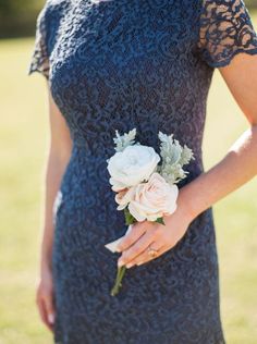 a woman in a blue dress holding a white rose and greenery boutonniere