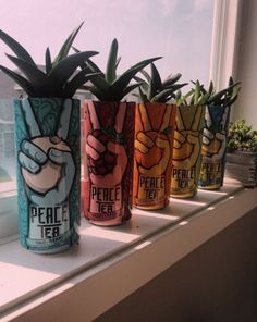 four cans with plants in them sitting on a window sill next to a potted plant