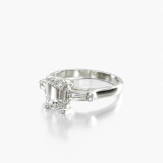 18K White Gold Tapared Baguette Three Stone Diamond Engagement Ring. Two tapered baguette side stones gracefully raise the emerald cut center stone of your choice to complemeny and enhance the elegant lines and reflections of this timeless engagement ring.