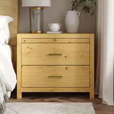 a wooden dresser with two vases on top of it next to a white bed