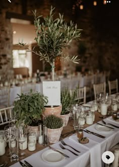 the table is set with white linens, silverware and greenery in vases