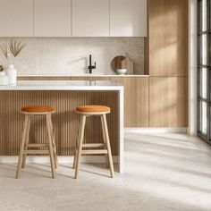 two wooden stools sit in front of an island with white countertops and cabinets