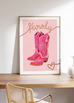 a pink cowboy boot sits on a desk next to a white vase and framed photograph