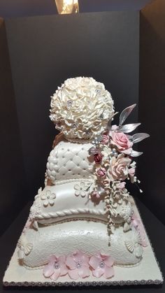 a three tiered wedding cake decorated with flowers and pearls on the top, sitting on a black table