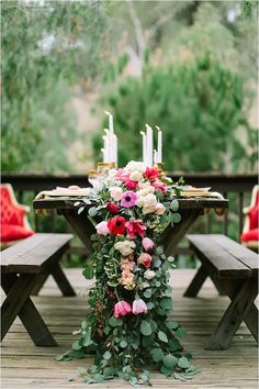 an outdoor table with flowers and candles on it, surrounded by red velvet chairs in the background