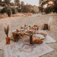 a table set up with candles, plates and pillows on a rug in the middle of a field