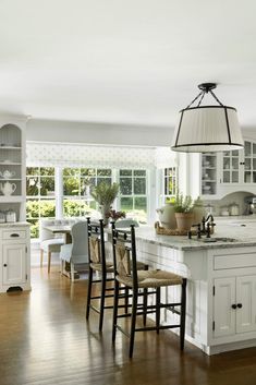 a large kitchen with white cabinets and wooden floors is pictured in this image, there are several chairs around the island