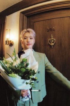 a woman holding a bouquet of flowers standing in front of a wooden door with a light green suit on