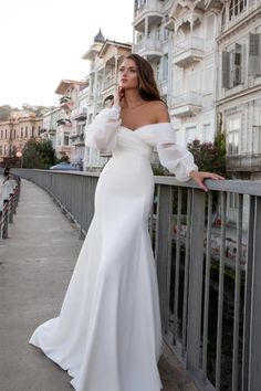 a woman in a white dress leaning on a fence and talking on her cell phone