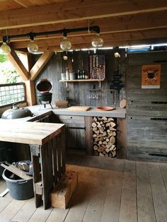 an outdoor kitchen with wood stacked on the floor and lights hanging from the ceiling above it