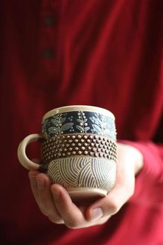 a person is holding two cups in their hands, one with designs on it and the other without