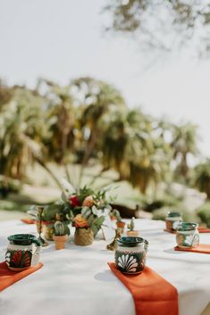 the table is set with orange napkins and green vases on top of it