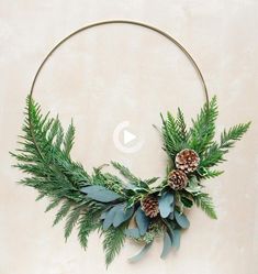 a circular wreath with pine cones and evergreen leaves is hung on the wall, surrounded by greenery