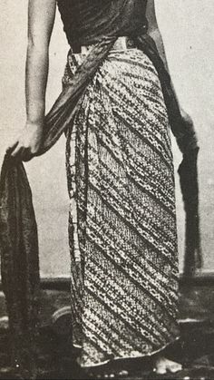 an old black and white photo of a woman in a skirt holding a purse with her right hand