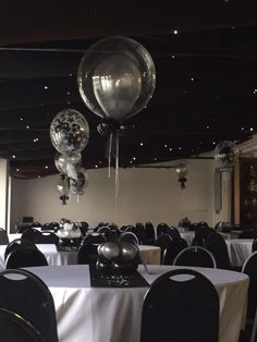 balloons are hanging from the ceiling in an empty room with white tablecloths and black chairs