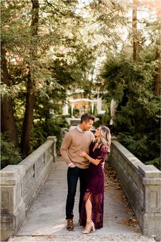 an engaged couple standing on a bridge in front of some trees and bushes during their engagement session