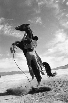 a man riding on the back of a horse across a desert field under a cloudy sky