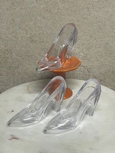 two clear high heels sitting on top of a white marble table next to an orange plate