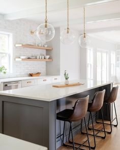 a kitchen island with four bar stools in front of it and hanging lights above