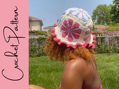 a woman sitting in the grass wearing a crocheted hat with flowers on it