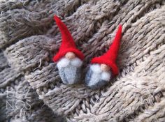 two small red and white gnomes sitting on top of a gray knitted blanket