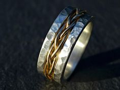 two gold and silver wedding bands with twisted wire on each side, sitting on a black surface