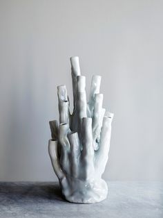 a white ceramic sculpture sitting on top of a table next to a gray wall and floor