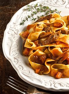 a white plate topped with pasta and meat covered in sauce on top of a wooden table