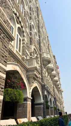 the building has many windows and arches on it's sides, along with people walking down the sidewalk