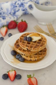 two waffles with butter and blueberries on a plate next to strawberries