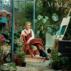 a woman sitting in a chair surrounded by potted plants and other things on the ground