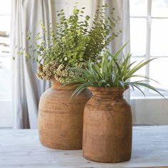 two vases with plants in them sitting on a table next to a window sill