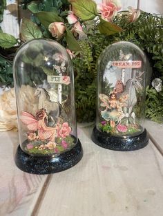 two glass cloches with fairy figurines under them on top of a table