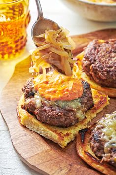 a wooden cutting board topped with burgers covered in cheese