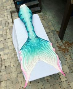 a large blue and pink mermaid tail laying on top of a white sheet covered bench