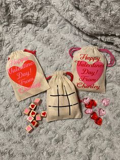 three valentine's day candy bags on a bed with hearts and marshmallows