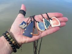 a person's hand holding five different colored stone pendants in their left palm