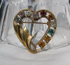 "This looks very similar to the brooch put out by Catamore in the 1940's, however it does not have their signature. That particular one is usually marked 12K GF, whereas this one is marked 18K HGE (hard gold electroplate). This pretty brooch measures 1 & 3/8\" wide and is also 1 & 3/8\" from top to bottom. Multiple colored prong set rhinestones with no missing stones. Two of the ribbon swirls have texture, there are no finish issues. Rolling \"c\" clasp. Very sweet and beautiful!" Antique Heart Brooch For Wedding, Vintage Heart-shaped Collectible Brooch, Vintage Heart Shaped Collectible Brooch, Collectible Vintage Heart-shaped Brooch, Antique Heart-shaped Wedding Brooch, Vintage Brooch For Valentine's Day Formal, Vintage Heart-shaped Wedding Brooches, Vintage Wedding Brooches For Valentine's Day, Vintage Gold Heart Brooches