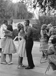 an old black and white photo of two people hugging each other in front of a group of people