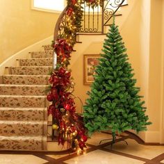 a christmas tree sitting in front of a stair case next to a decorated christmas tree