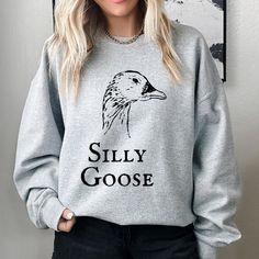 "Introducing our \"Silly Goose\" Gray Sweatshirt by Gildan 18000 - a playful and whimsical addition to your wardrobe that's bound to bring smiles wherever you go. This cozy sweatshirt combines comfort and humor in a classic design that's perfect for all ages. 🦢 Product Details: - Premium Comfort: Crafted with the renowned Gildan 18000 sweatshirt, this cozy pullover is soft, warm, and perfect for chilly days. - Silly Goose Design: The charming image of a goose's head, paired with the words \"Silly Goose\" in an old-fashioned font, adds a touch of humor and nostalgia to your attire. - Classic Gray: The neutral gray color of the sweatshirt makes it easy to pair with jeans, leggings, or your favorite bottoms. - Durable and Versatile: Whether you're lounging at home or stepping out for some fu Novelty Cotton Crew Neck Sweatshirt, Funny Crew Neck Sweatshirt With Print, Funny Crew Neck Sweatshirt With Screen Print, Silly Goose University, Goose Design, Gift For Guys, Funny Goose, University Crewneck, Funny Gifts For Men