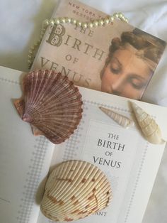 the birth of venus book and seashells on a white bed sheet with pearls