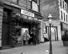 two people standing in front of a store on a street corner next to a lamp post