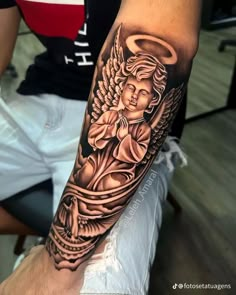 a man with a black and grey tattoo on his arm is holding an angel in his hand