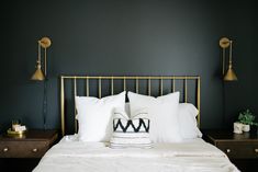 a bed with white pillows and two lamps on each side, along with a black wall in the background